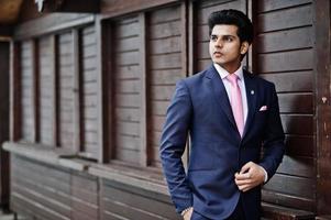 Elegant indian macho man model on suit and pink tie posed against wooden stalls. photo