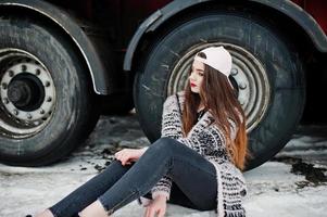 Brunette stylish casual girl in cap sitting against truck wheels. photo
