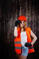 Engineer woman in orange protect helmet and building jacket against wooden background. photo