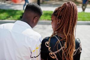 Handsome stylish african american couple with mobile phones at hands sitting on bench at city. photo