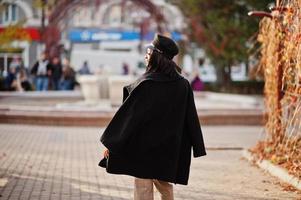 chica de moda afroamericana con abrigo y gorra de repartidor de periódicos posada en la calle. foto