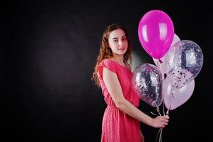 Young girl in red dress with balloons against black background on studio. photo
