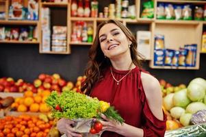 Girl in red holding different vegetables on fruits store. photo