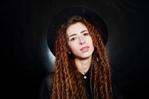 Studio shoot of girl in black with dreads and hat at black background. photo