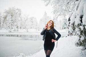 Red haired girl in fur coat walking at winter snowy park. photo