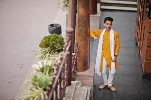 hombre indio con estilo en ropa tradicional amarilla con bufanda blanca posada al aire libre. foto