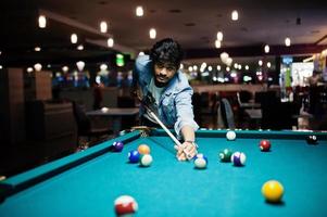 Stylish asian man wear on jeans playing pool billiard on bar. photo