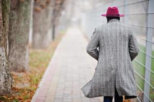 Back of walking stylish African American man model in gray coat and red hat. photo