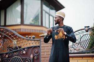 Rich african man in stylish traditional clothes and hat posed outdoor background his mansion. photo