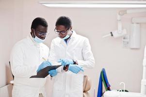 Two african american male colleagues doctors working together, discussing and looking at clipboard on clinic. photo