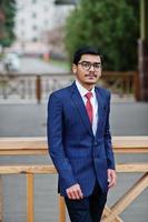 Indian young man at glasses, wear on suit with red tie posed outdoor. photo