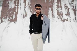 Casual young indian man in black shirt and sunglasses with jacket on shoulders posed at winter day. photo