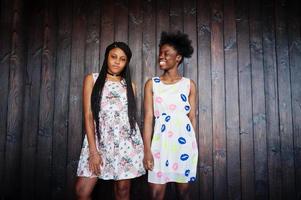 dos novias africanas negras con vestidos de verano posaron sobre un fondo de madera oscura. foto