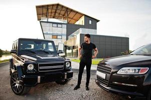 Asian man wear on all black posed near suv car. photo