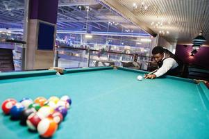 Young handsome african man wearing white shirt, black vest and bow tie play pool billiard. photo