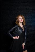 Curly hair girl at leather jacket on studio against black brick wall. photo