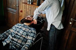 apuesto hombre barbudo en la barbería, peluquero en el trabajo. cabezal de lavado. foto