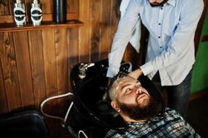 Handsome bearded man at the barbershop, barber at work. Washing head. photo