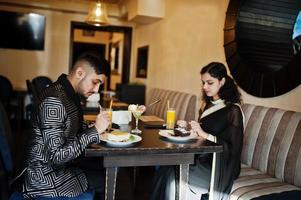 Lovely indian couple in love, wear at saree and elegant suit, sitting on restaurant and eating desserts together. photo