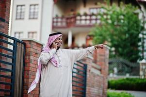 hombre de negocios árabe del medio oriente posó en la calle contra un edificio moderno con teléfono móvil y mostrando el dedo. foto