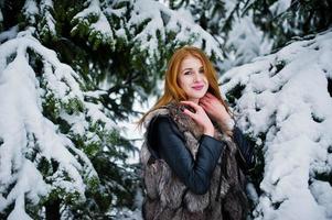 chica pelirroja con abrigo de piel caminando en el parque nevado de invierno. foto