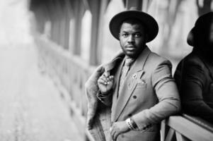 Stylish African American man model in gray coat, jacket tie and red hat posed at foggy weather street. Black and white photo. photo