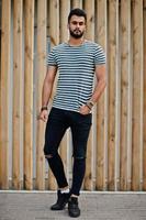 Handsome tall arabian beard man model at stripped shirt posed outdoor against wooden background. Fashionable arab guy. photo