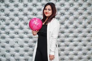 Stylish asian woman with pink bowling ball at hand against silver wall background. photo