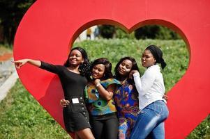 grupo de cuatro chicas afroamericanas contra un gran corazón rojo al aire libre. foto