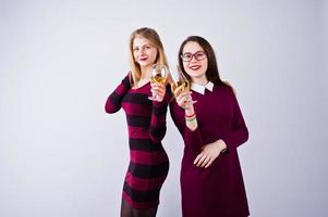 Two attractive friends in purple dresses drink sparkling wine or champagne in the studio. photo