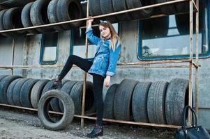 Young hipster girl in jeans jacket and head scarf at tire fitting zone. photo