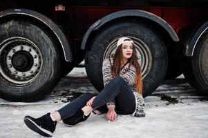 Brunette stylish casual girl in cap sitting against truck wheels. photo