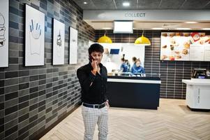 hombre indio hablando por teléfono móvil mientras espera su pedido en el café de comida rápida. foto