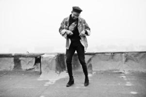 African american man in jeans jacket, beret and eyeglasses posed on abandoned roof. photo