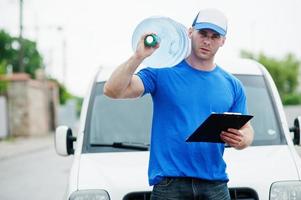 Delivery man with clipboard in front cargo van delivering bottles of water. photo