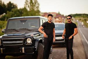 dos hermanos asiáticos se visten de negro y posan cerca de los autos todoterreno. foto