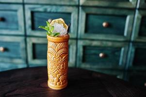 Alcoholic cocktail with mint in originally voodoo earthen glass on bar table. photo