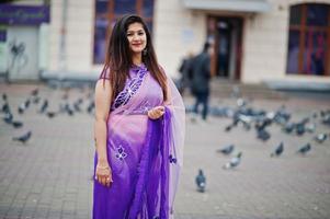 niña hindú india en el tradicional sari violeta posó en la calle contra las palomas. foto