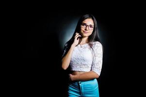 Portrait of an attractive young woman in white top and blue pants posing with her glasses in the dark. photo