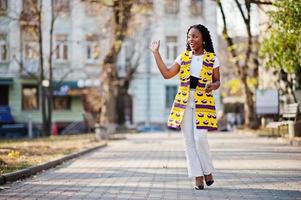 Stylish african american women in yellow jacket posed on street at sunny day with mobile phone at hand. photo