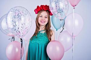 Happy girl in green turqoise dress and wreath with colored balloons isolated on white. Celebrating birthday theme. photo