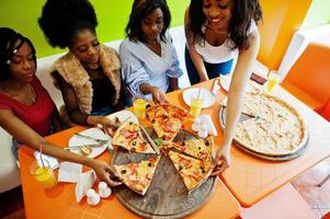 cuatro jóvenes africanas en un restaurante de colores brillantes comiendo pizza. foto