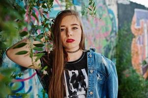 chica hipster casual con estilo en ropa de jeans y gafas contra una gran pared de graffiti. foto