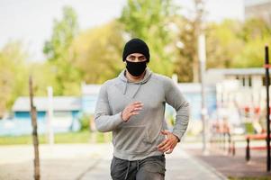 Portrait sports arabian man in black medical face mask run outdoor during coronavirus quarantine. photo