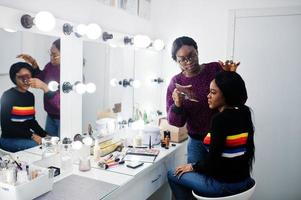 African American woman applying make-up by make-up artist at beauty saloon. photo