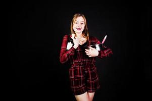 Young housewife in checkered dress with saucepan and kitchen spoon and bottle isolated on black background. photo