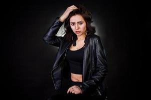 retrato de estudio de chica morena sexy en chaqueta de cuero negro sobre fondo negro. foto