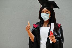 una joven estudiante graduada afroamericana usa una máscara protectora contra el coronavirus. concepto de ceremonia de graduación, cuarentena. foto