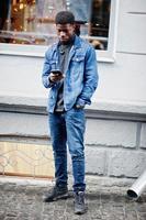 African man wear on jeans jacket posed outdoor with cell phone at hand. photo