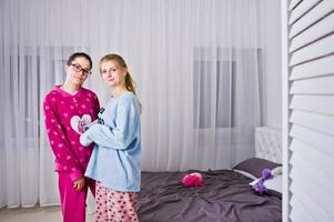 Two friends girls in pajamas having fun on bed at room. photo